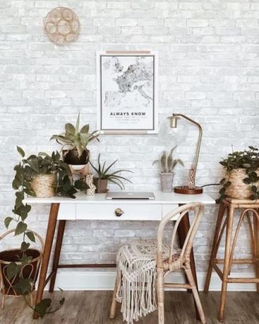 Eleganckie domowe biuro w stylu boho ze stołem z drewna retro, dywanikiem boho, ściennym rękodziełem, mnóstwem roślin doniczkowych: kaktusy i sukulenty